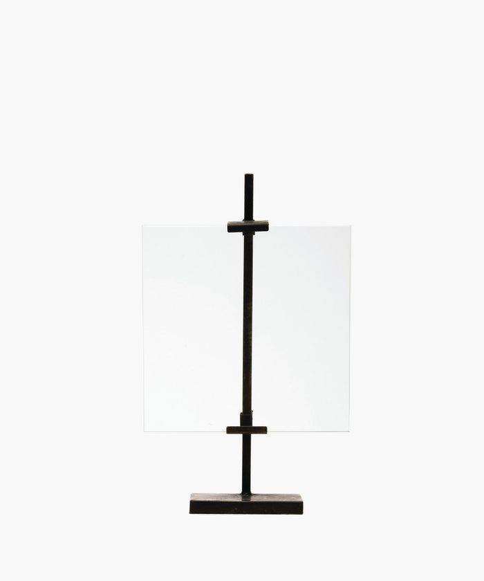 A minimalist black metal display stand with a vertical metal clamps holds a clear, rectangular glass sheet. The simple design exudes an industrial, modern feel. | SW Home