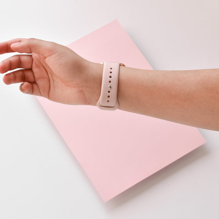 Powder pink Coconut Lane NAKD Fitbit strap worn on a hand, resting on a matching light pink rectangular surface.