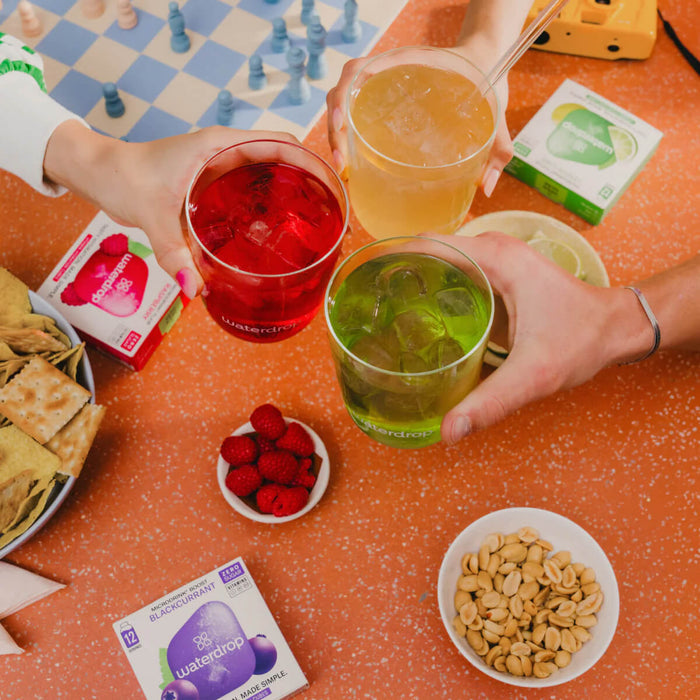 Three people holding drinks together at a table with snacks and a game board.
