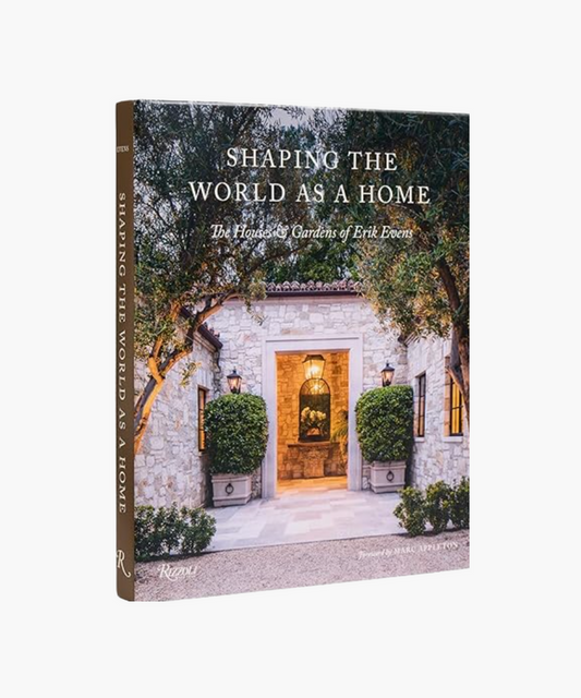 Book cover titled "Shaping the World as a Home," features a stone house entrance framed by lush greenery and lanterns, conveying elegance and warmth. | Wildwood Home Co.