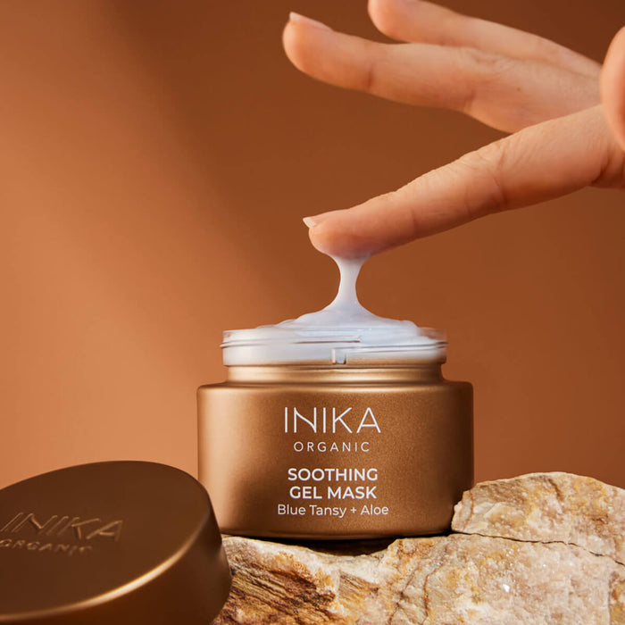 Finger dipping into open jar of soothing gel mask with blue tansy oil and aloe vera, showing the texture.
